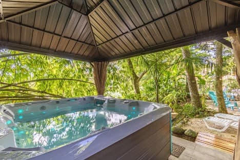 Outdoor hot tub under a pavilion roof surrounded by lush jungle greenery